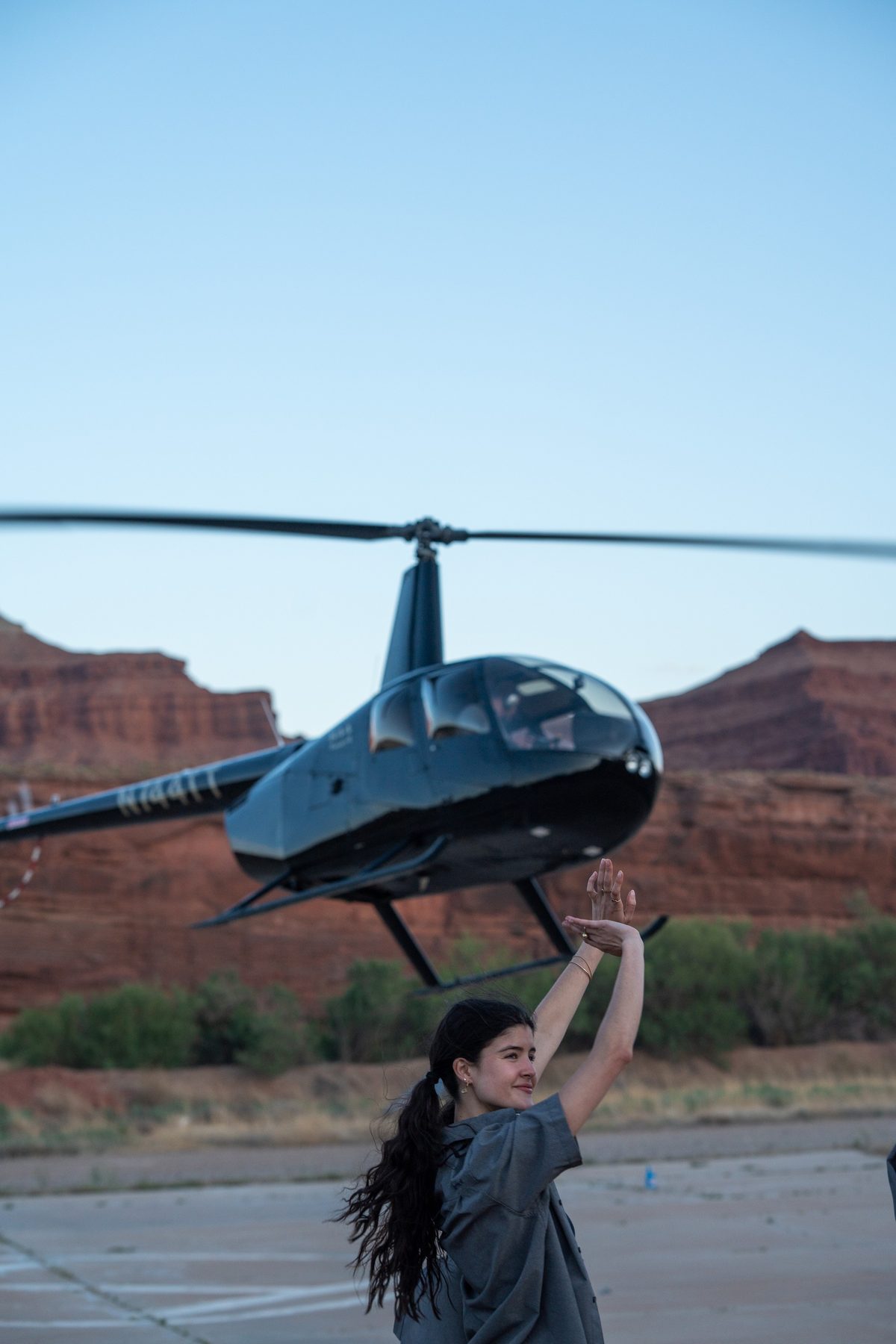 A guest waves as a helicopter lands against red cliffs