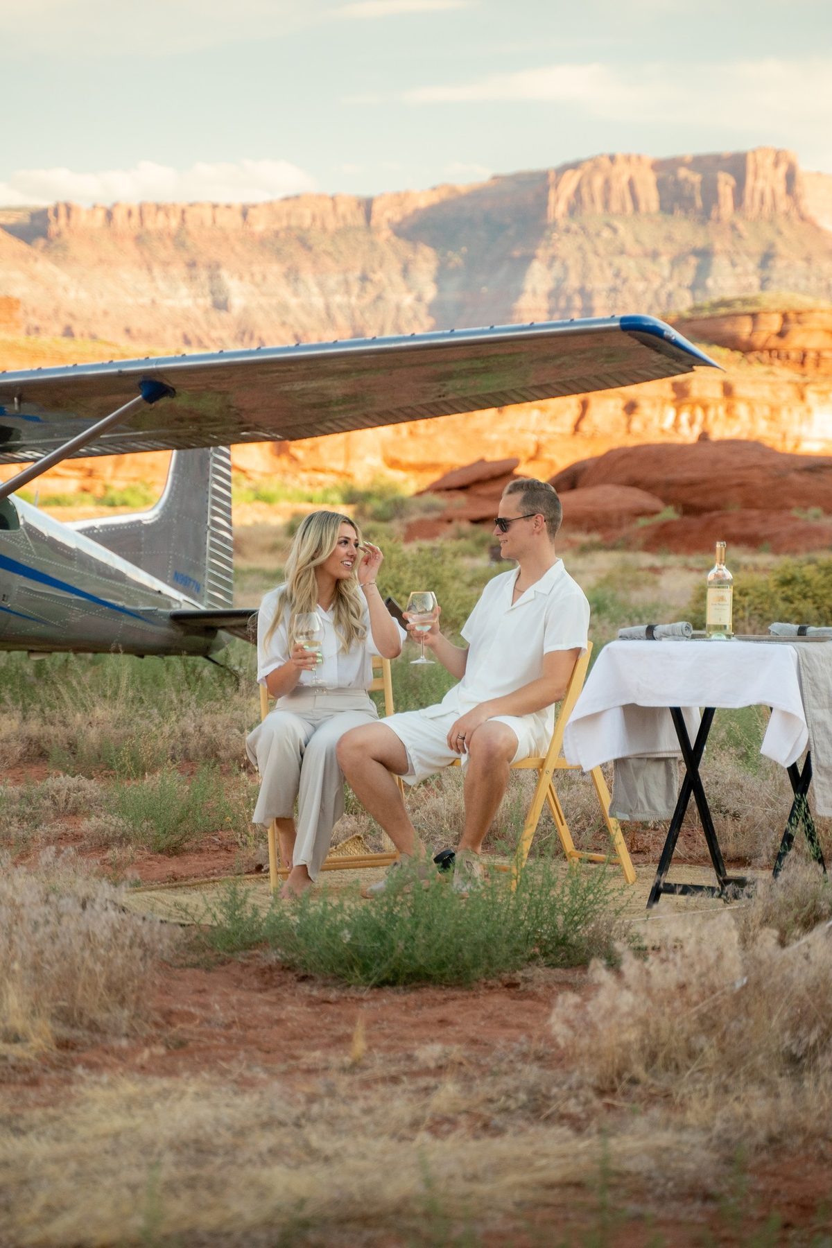 A couple at a dinner table set beside a parked aircraft in the desert