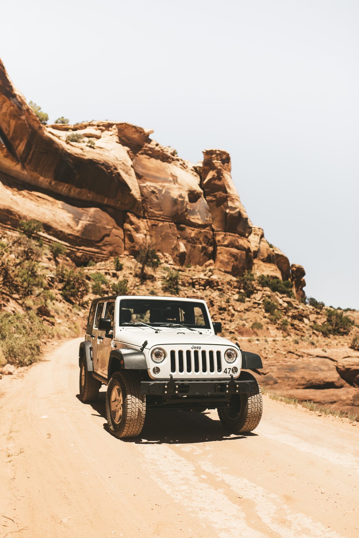 A white Jeep on a dirt road beneath sandstone cliffs