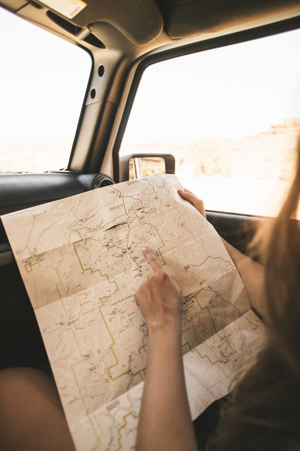 A hand tracing a route on a Canyonlands park map inside a Jeep