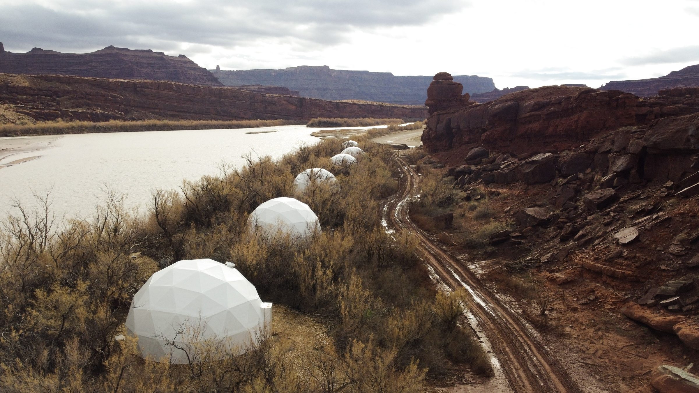 White guest domes along a river beneath canyon walls