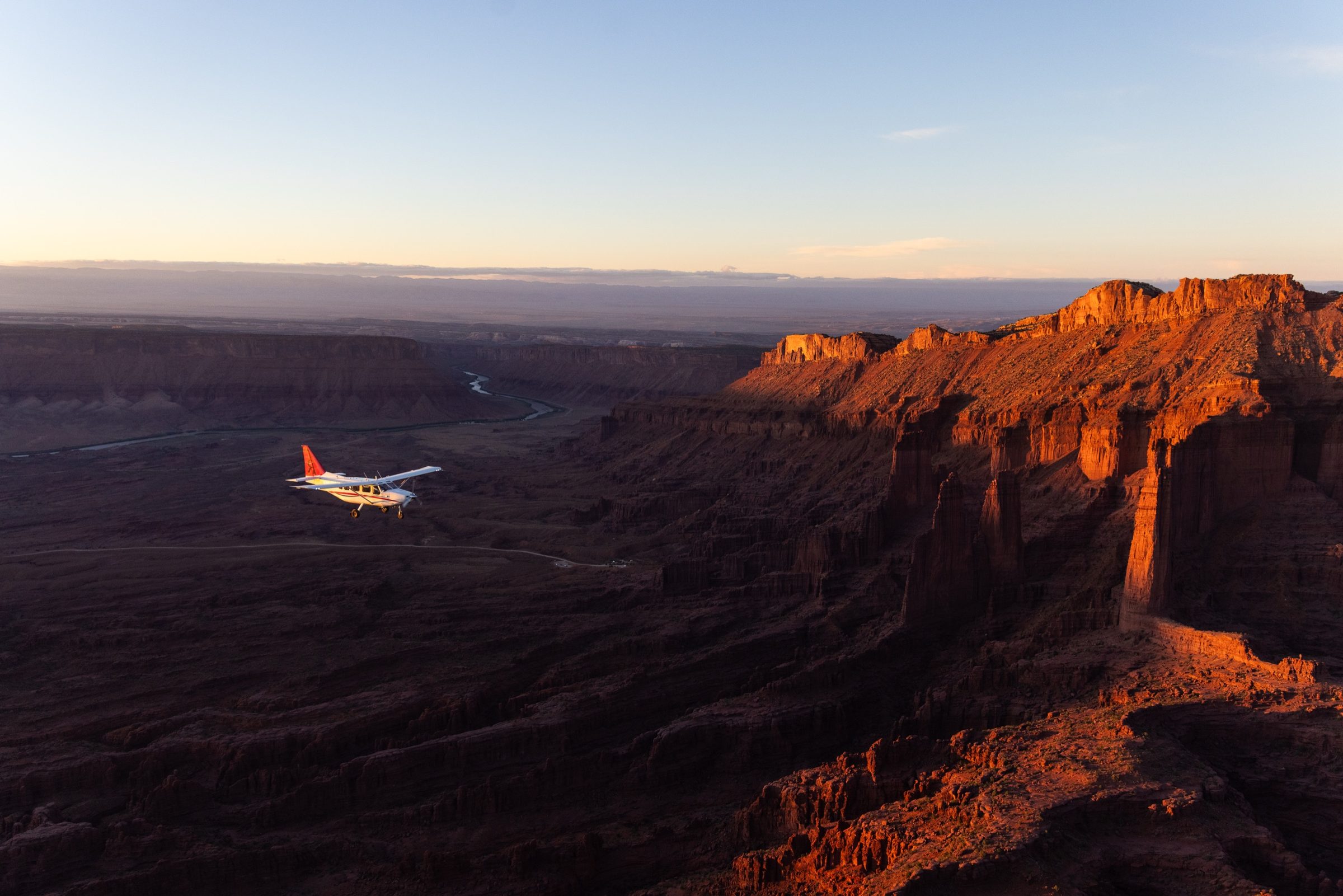 A small aircraft crossing a canyon at sunset, the mesa walls lit red