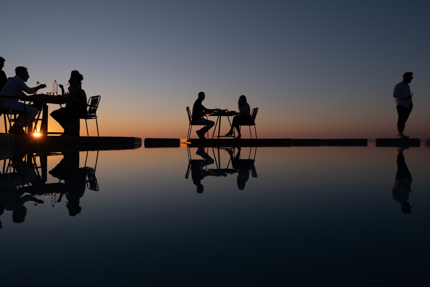 Guests dining at the edge of an infinity pool at sunset